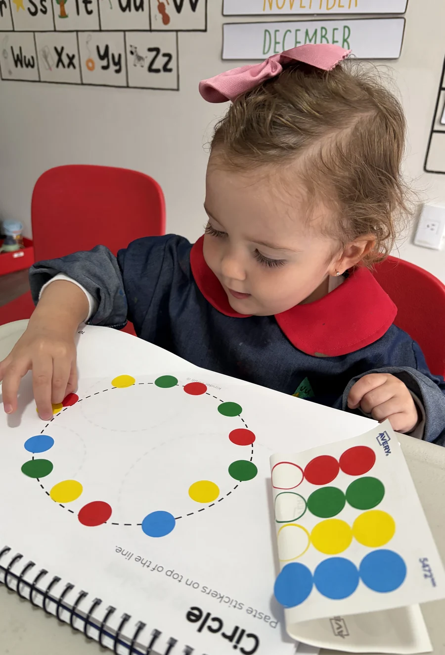 Niña de Pirulí con moño rosa pegando stickers de colores